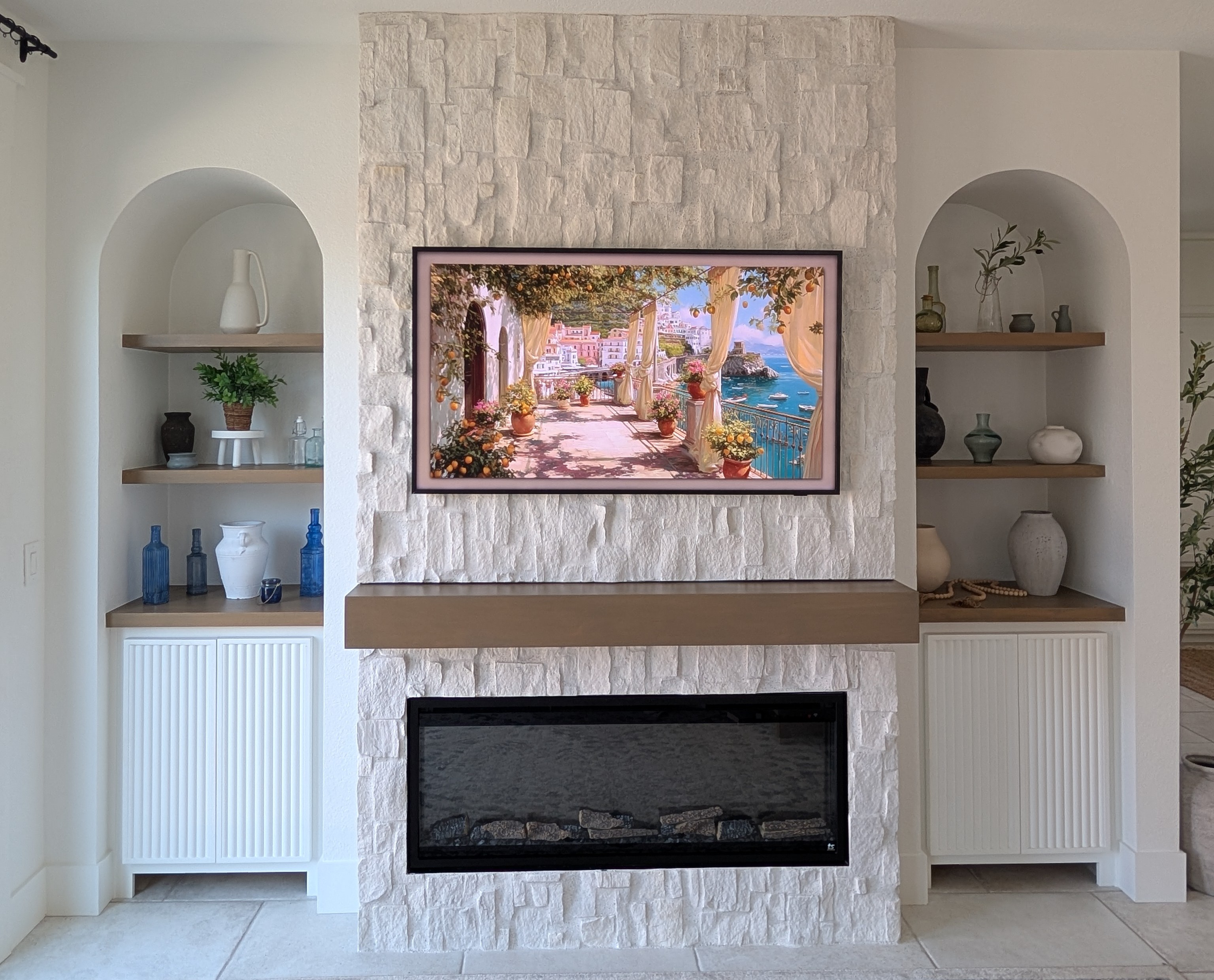 Finished stone fireplace wall with framed TV art, arched niches, floating shelves, and built-in cabinetry, Menifee CA