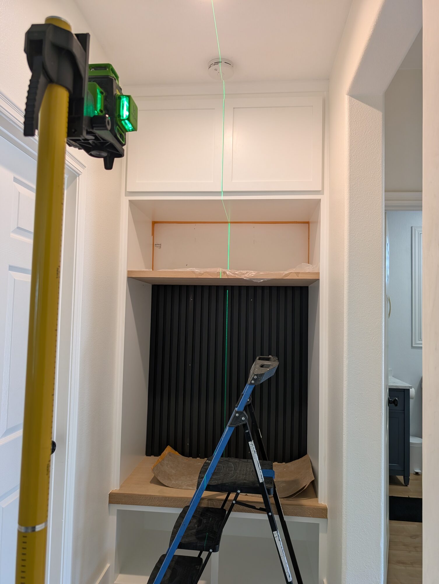 Green laser line setting the upper slat section plumb above the white oak shelf, Winchester CA
